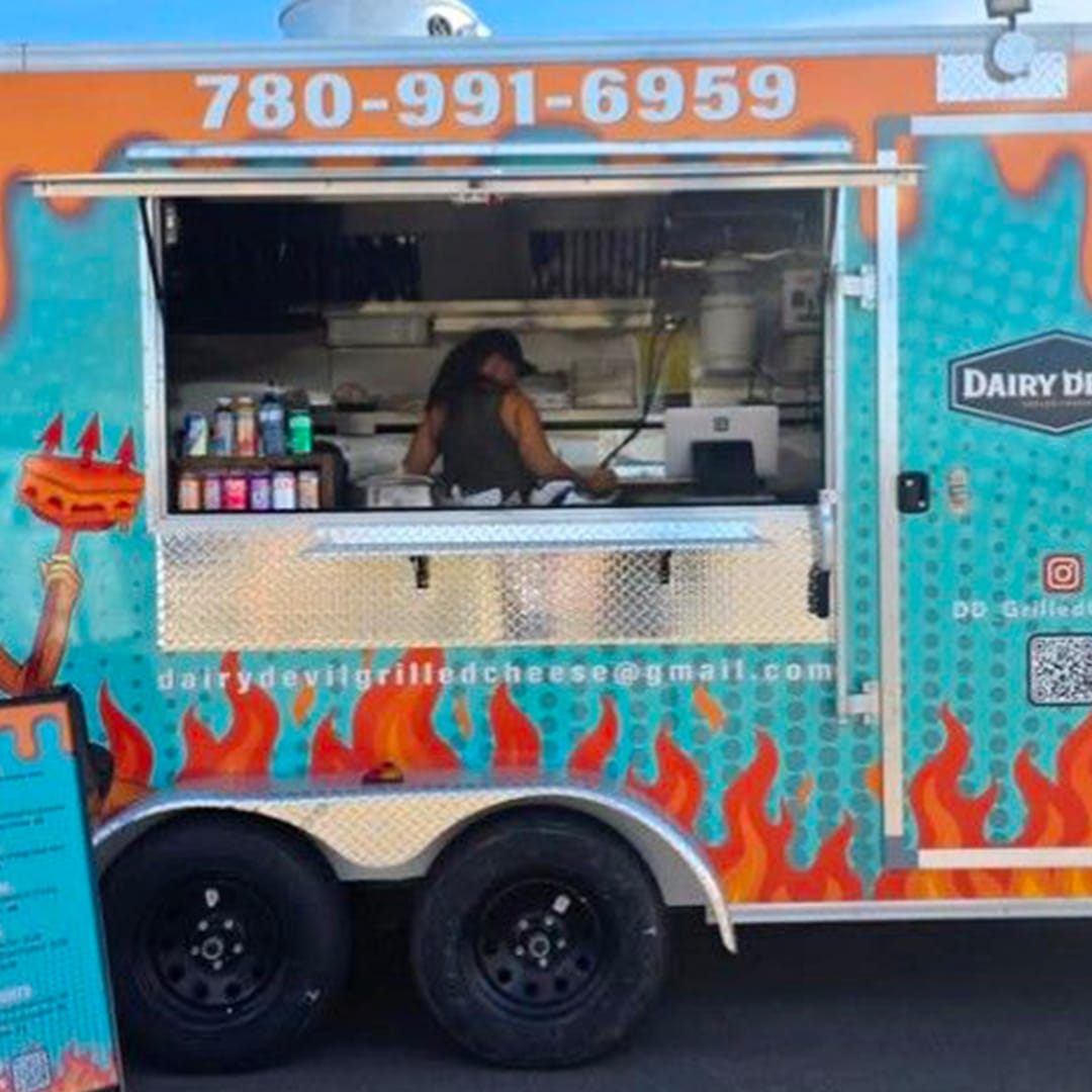 Colorful food truck with blue flames and orange fire graphics, service window open and a worker inside with condiments on the counter.