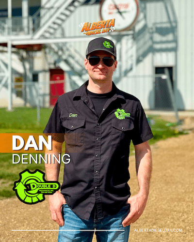Portrait of Dan Denning in a black logo shirt and cap, standing outdoors by an industrial building; his name is overlaid on the image.