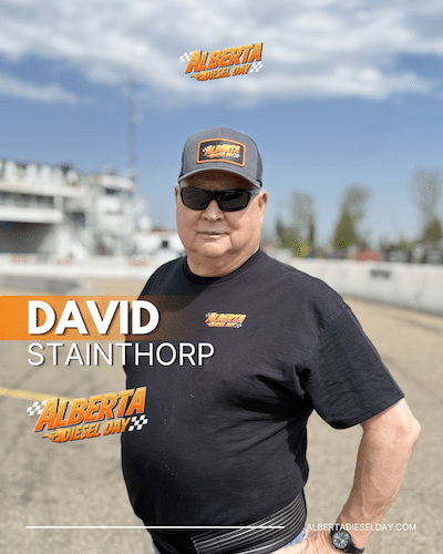 Portrait of a David wearing a cap and sunglasses at Alberta Diesel Day, standing on a race track with event logos visible on his shirt, cap, and in the background.